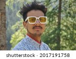 Closeup of a good looking young guy standing outdoor in the nature and wearing sunglasses with looking at camera 