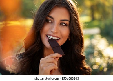 Closeup Of Gorgeous Elegant Young Woman Eating Dark Chocolate In The Park 