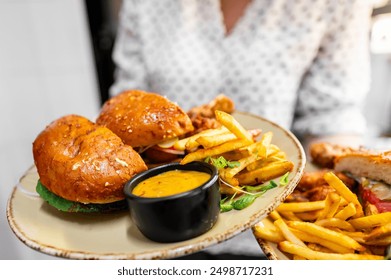 Close-up of a gourmet burger with fries and sauce on a plate, held by an individual in a polka dot shirt, suggesting a casual dining experience. Perfect for food and lifestyle themes. - Powered by Shutterstock