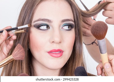 Closeup Of Gprgeous Blond Girl Getting Hair And Makeup Done By Many Hands Isolated Over White