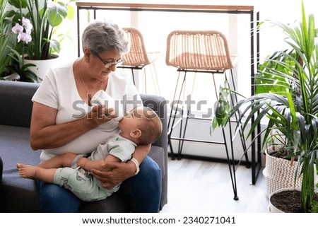 Close-up of a grandmother feeding a bottle to her baby grandchild at home