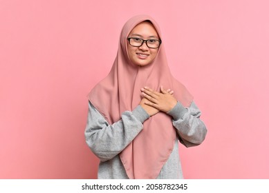 Close-up grateful, Muslim Asian woman feeling touched and flattered, smiling and gazing with affection, touch heart, express gratitude and delight of receiving nice gift, isolated on pink background