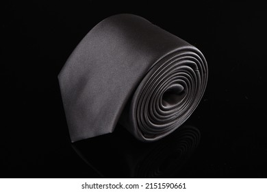 A Closeup Of A Gray Male Satin Necktie Roll Isolated On Black Background