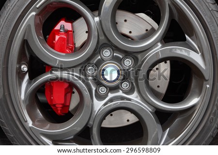 Close-up of gray, painted light weight, alloy wheel with a modern design featuring large circles. The red brake calipers stand out. Drilled disc brake. Low profile sports car tires. Alfa Romeo 4c.