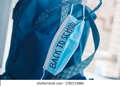 closeup of a green bookbag and a blue surgical mask with the text back to school written in it, depicting the need to prevent the infection at school in the covid-19 pandemic situation