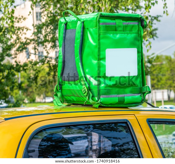 Closeup of green food delivery box, backpack\
standing on the top of yellow car. Mockup for food delivery\
service. Copy space.