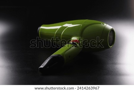 Close-up of green hairdryer, brand new device lay on dark background, instrument for beauty master. Last model to dry hair. Barbershop, technology concept