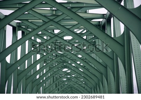 a closeup of the green metal beams of a bridge criss crossing in a pattern above the road below