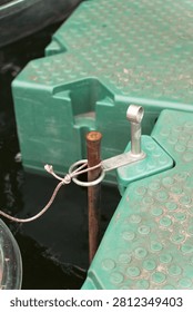 Close-up of a green modular plastic floating dock secured to a rusty metal pole with a rope knot in dark water