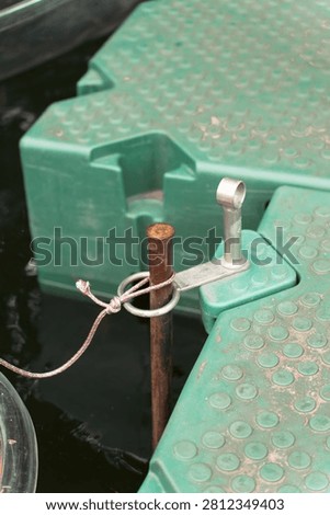 Close-up of a green modular plastic floating dock secured to a rusty metal pole with a rope knot in dark water