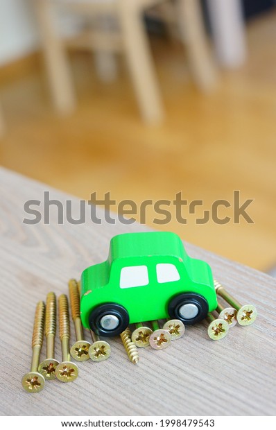 A closeup of a green painted wooden car toy on\
metal screws