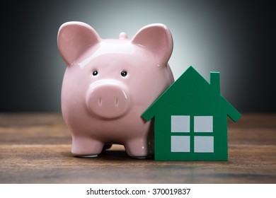 Closeup of green paper house and piggybank on wooden table against gray background - Powered by Shutterstock