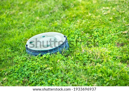 Closeup of green plastic pipe with cover on green grass lawn.