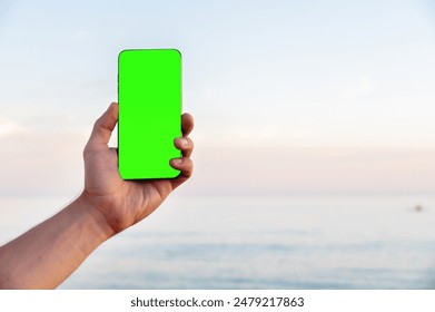 Close-up green screen Caucasian man holding a regular smartphone in his left hand, ocean beach in the background. High quality photo. Smartphone screen mockup cut out - Powered by Shutterstock