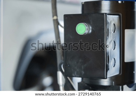 Close-up of green start push button switch on black electric motor control box of hydraulic car lift in auto repair garage, Green Start Button on Control Box, Power on Operation Control Energy