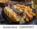 Closeup of grilled bratwurst and sauerkraut on a bun with french fries on a black plate