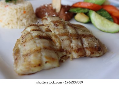 A Closeup Of Grilled Fish Entree With Rice Pilaf And Fresh Vegetables