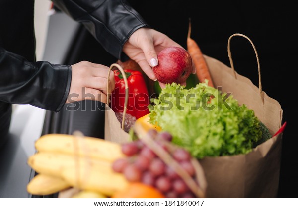Close-up of groceries in eco package in car\
trunk. Hands of female packing vegetables and fruits after shipping\
in supermarket