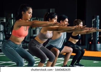 Close-up Of Group Of Athletic Young Asian People In Sportswear Doing Squat And Exercising At The Gym. Intense Workout And Healthy Lifestyle Concept