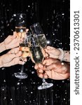 Closeup of group of friends toasting with champagne glasses at party against glittering background with confetti
