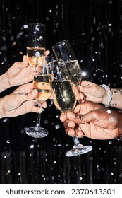 Closeup of group of friends toasting with champagne glasses at party against glittering background with confetti