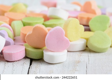 Closeup of a group of pastel candy Valentine's hearts on a rustic white wood table. Horizontal format.