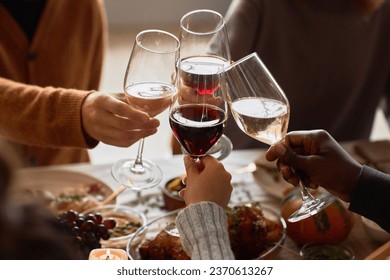 Closeup of group of people toasting with wine glasses at festive dinner table celebrating Thanksgiving together, copy space - Powered by Shutterstock