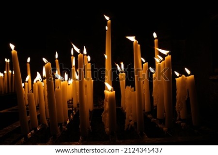 Closeup of group white yellow wax candles burning in the wind, dark black background in church (focus on candles in front center)