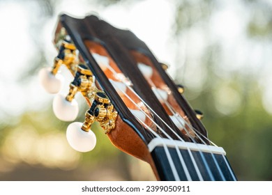 Close-up of the guitar head of a classical guitar with gold pegs. Part of a classical guitar on a blurry background in the park. Head of guitar with nylon strings. - Powered by Shutterstock