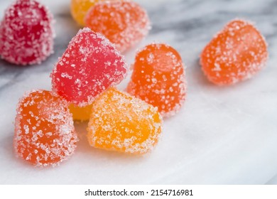 Closeup Of Gummy Candy Gumdrops In Red, Yellow, And Orange On A White Marble Surface. Vitamin Supplement Or CBD Edibles.