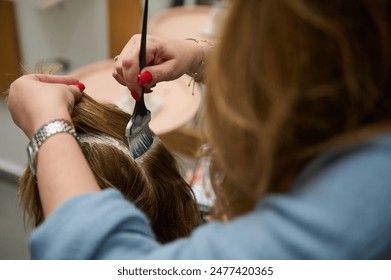 Close-up of hairdresser applying dye to client's hair in a beauty salon. Hands holding brush in hair coloring process. - Powered by Shutterstock