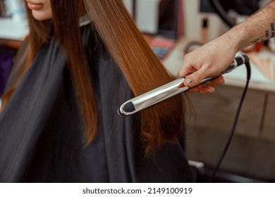 Closeup Of Hairdresser Hand Holding Hair Straightener. Beauty Salon Services Concept