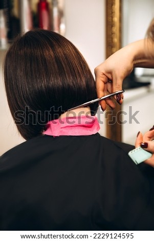 Close-up of the hairdresser's hands cutting the bob of a girl with dark hair. Back view