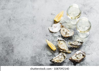 Close-up of half dozen of fresh opened oysters and shells with lemon wedges, two glasses of white wine or champagne, top view, grey rustic concrete background, space for text. Romantic or celebration