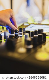 Close-up of a hand adjusting knobs on a professional audio mixing console, with vibrant lights in the background, capturing a dynamic music production environment.