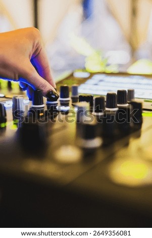 Close-up of a hand adjusting knobs on a professional audio mixing console, with vibrant lights in the background, capturing a dynamic music production environment.