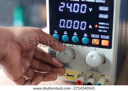 Close-up of a hand adjusting the voltage or current knob on a digital laboratory DC regulated power supply unit.