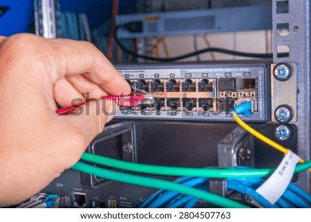 closeup of hand of administrator connecting network cable into switch