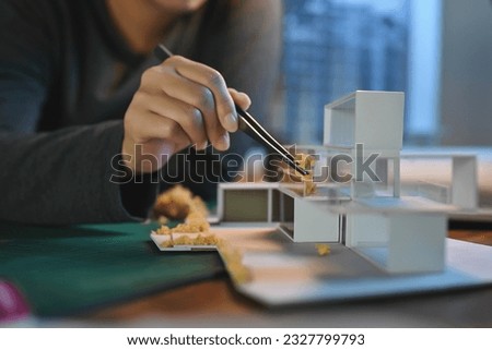 Close-up hand of Architect students diligently make house model building samples with paper art architecture tools at night in their alone room.