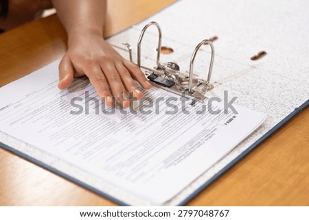 Close-up of a hand arranging paperwork inside a ring binder folder. Concept of document management, filing system, office organization, and administration.