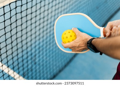 A close-up of a hand of an athlete with a pickleball racket and a ball about to make a serve. Pickle ball concept. Sports that are played with rackets.