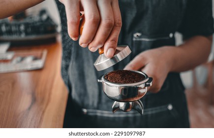 Close-up of hand barista or coffee maker holding portafilter and coffee tamper making an espresso coffee. - Powered by Shutterstock