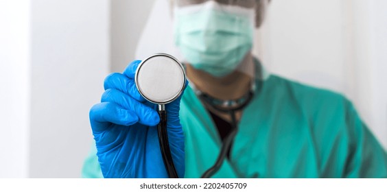 Closeup hand in blue glove holding stetoscope, male medical doctor wearing surgery uniform and surgical mask showing stethoscope to camera in clinic , selective focus