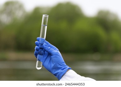 Close-up of a hand in a blue glove holding a glass test tube full of river water samples for analysis, a concept on the topic of checking water quality in reservoirs - Powered by Shutterstock