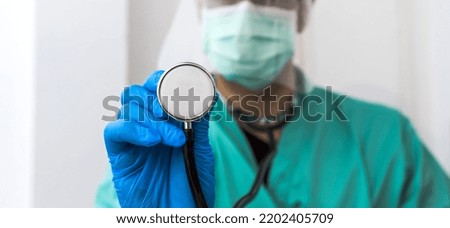 Closeup hand in blue glove holding stetoscope, male medical doctor wearing surgery uniform and surgical mask showing stethoscope to camera in clinic , selective focus