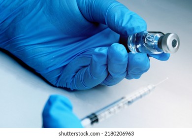 Close-up Of A Hand In A Blue Medical Seal Holding A Vial Of A Vaccine. In The Foreground, The Syringe Is Out Of Focus. The Concept Of The Fight Against Covid19.