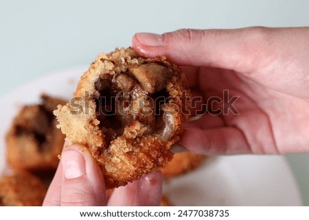 Close-up of a hand breaking open a crispy Japanese curry bun to reveal the succulent meaty filling inside