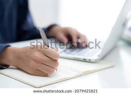 Closeup hand of business man writing on note while using laptop computer on desk at home, male planning on note for business success, author and blog, businessman working on table, employee and job.