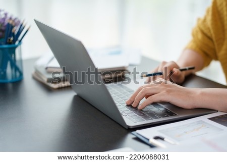 Close-up of hand of businesswoman working together using laptop computer to record and print information for a marketing plan analyze the balance sheet report quarterly financial statement.