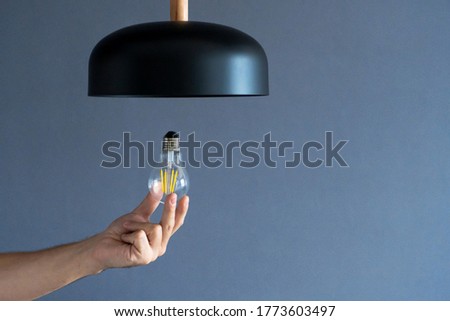 Close-up. A hand changes a light bulb in a stylish loft lamp. Spiral filament lamp. Modern interior decor
